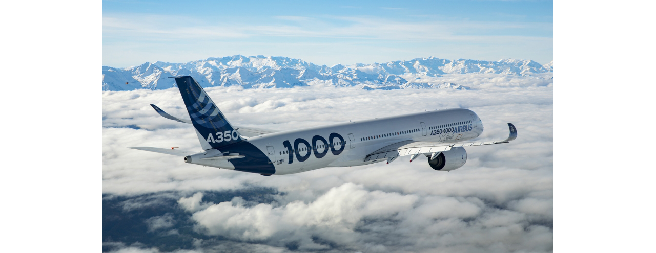 Side view of an Airbus A350-1000 widebody aircraft flying above the clouds with mountains in the background  