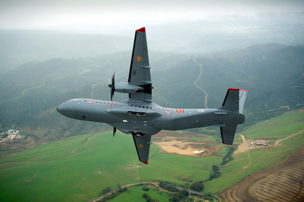 An Airbus C295 transport aircraft banks while flying over a mountainous region in South America. 