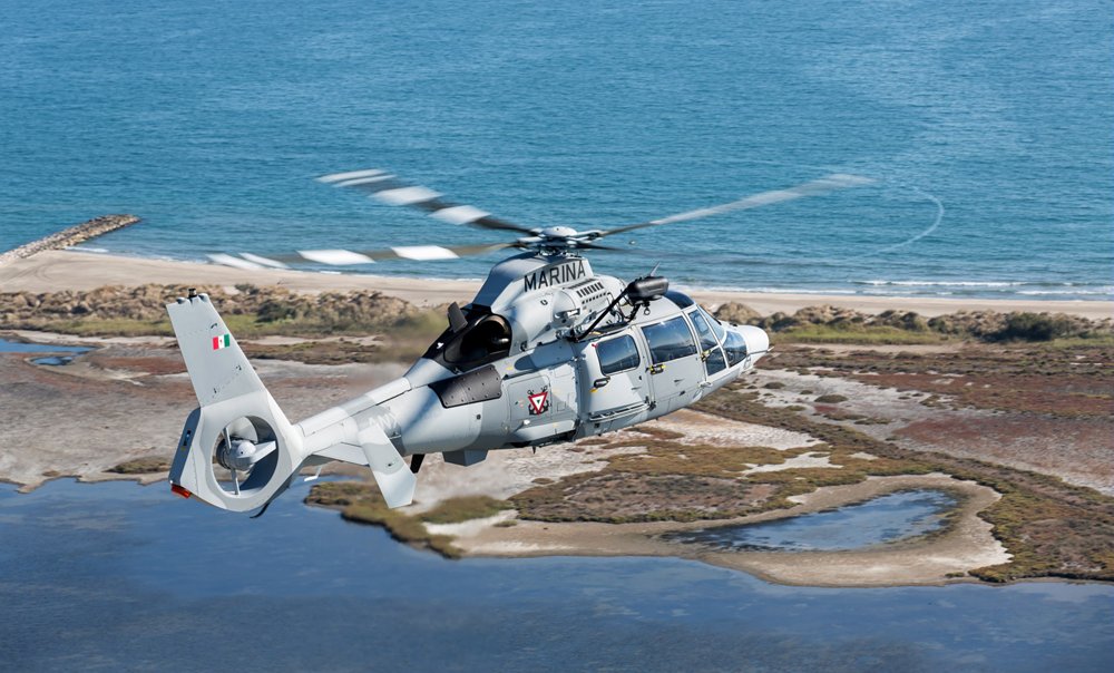 An in-flight Airbus AS565 MBe military helicopter shown over coastal terrain. 