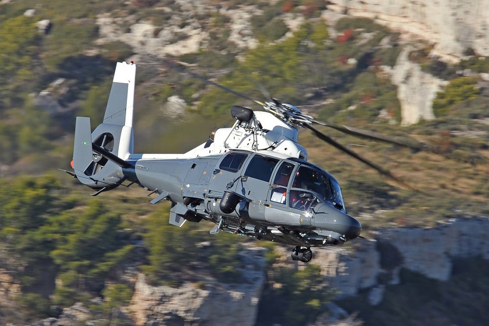 Side view of an Airbus AS565 MBe military helicopter banking over mountainous terrain. 