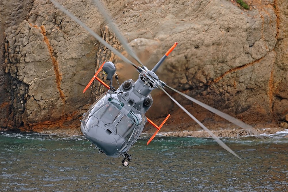 An Airbus AS565 MBe military helicopter flies over water. 