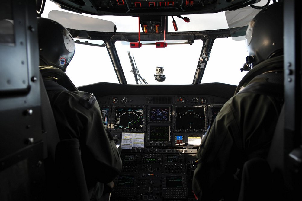 An “over the shoulder” photo of pilots inside the cockpit of an Airbus H225M military helicopter. 