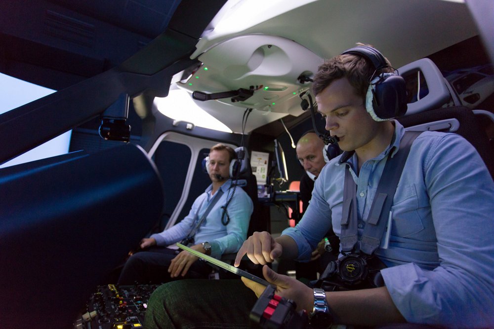 A helicopter pilot reviews digital documentation on a tablet device inside the cockpit. 