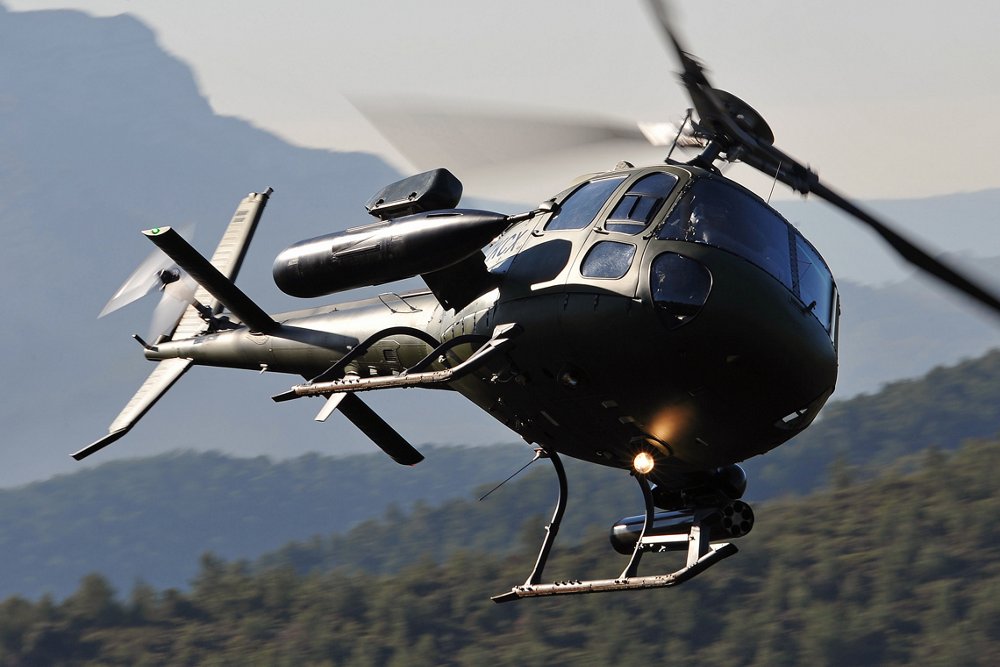 An in-flight Airbus H125M military helicopter is operated in mountainous terrain. 