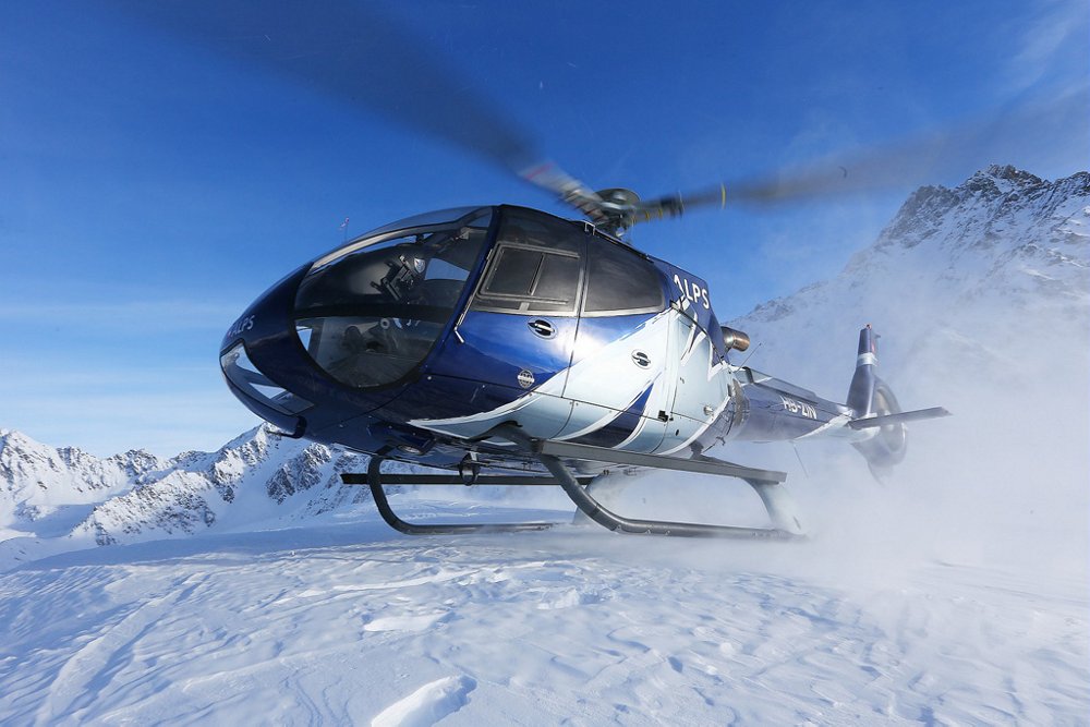An Airbus H130 helicopter touches down to land in snowy, mountainous conditions 