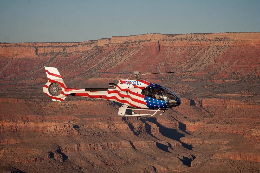 An H130 helicopter with distinctive U.S. flag livery flies over the Grand Canyon 
