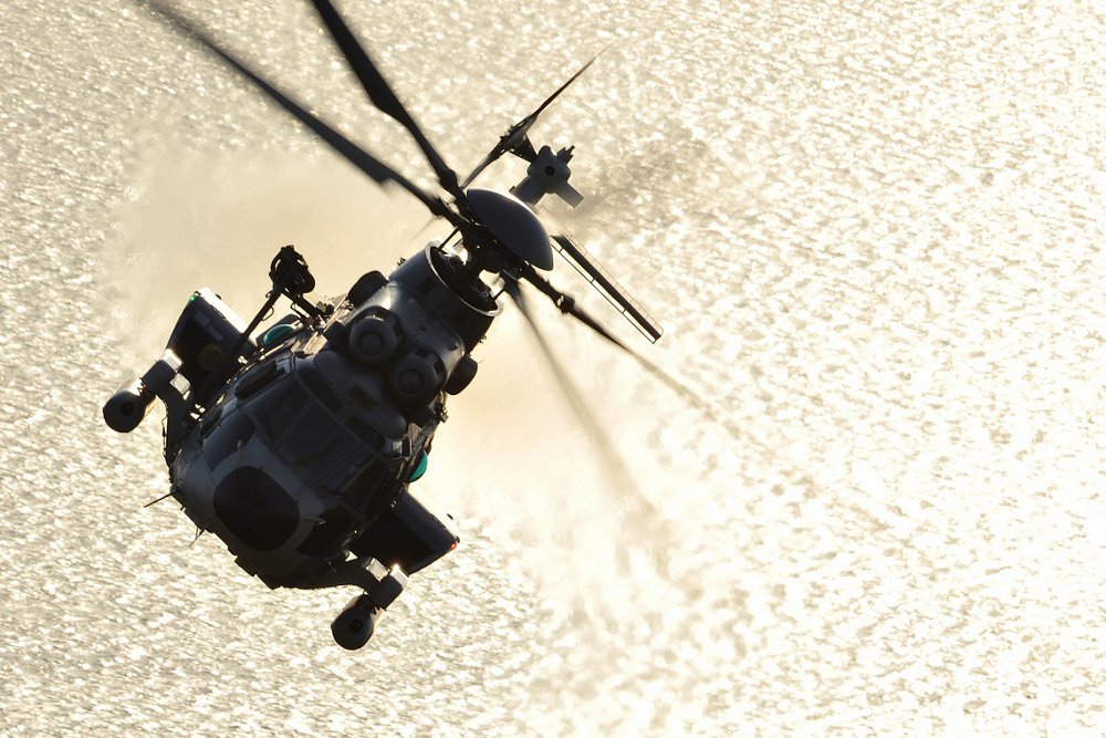 Head-on view of an Airbus H225M military helicopter banking over water.  
