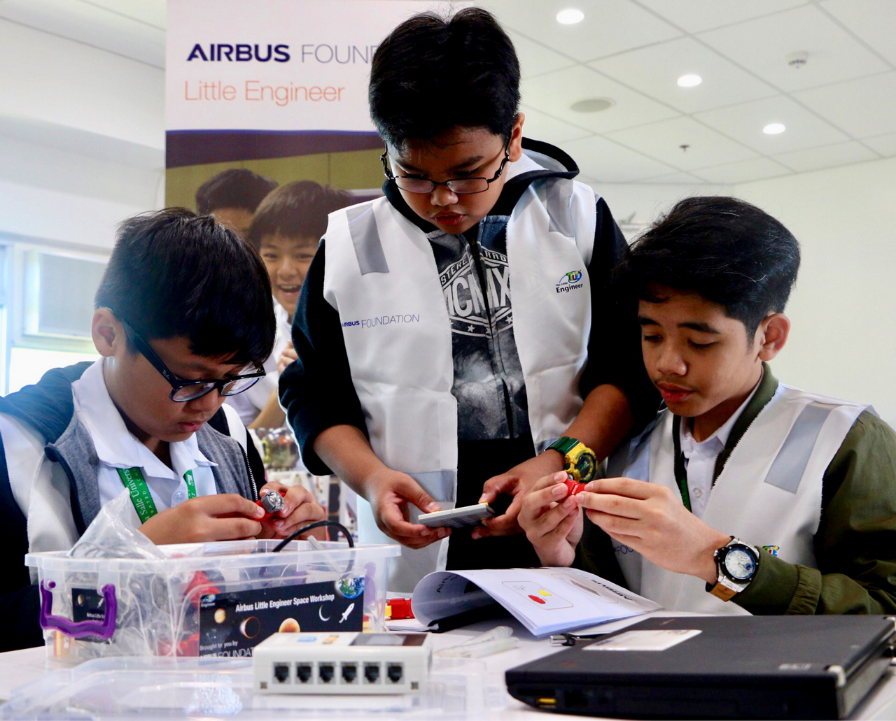 Three students collaborate during an Airbus Little Engineer workshop event in Singapore.