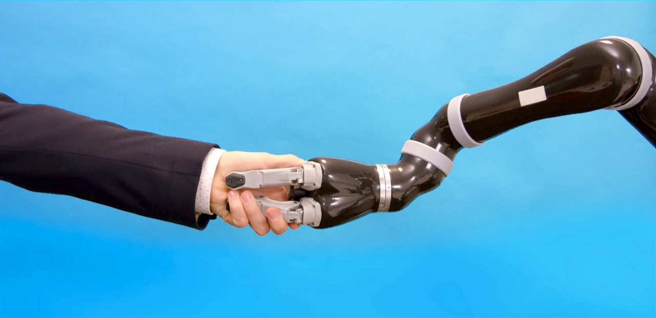 A human arm shakes hands with a robot arm.  