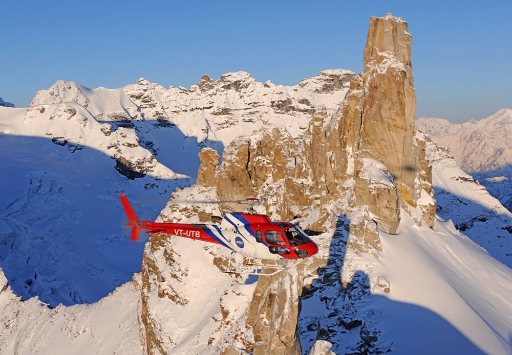 An Airbus H125 helicopter is operated above snow-covered, mountainous terrain  