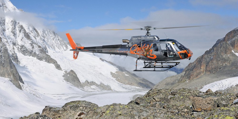 An Airbus H125 helicopter hovers above mountainous terrain 