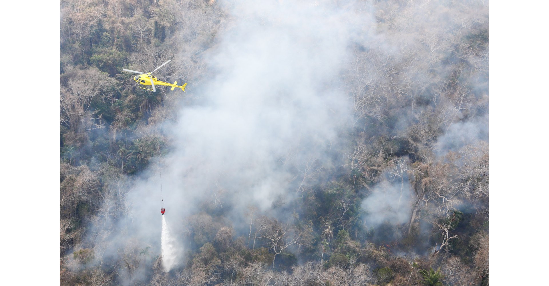 An H125 helicopter supports firefighting efforts with deployment of a bucket-type water dispersal system.