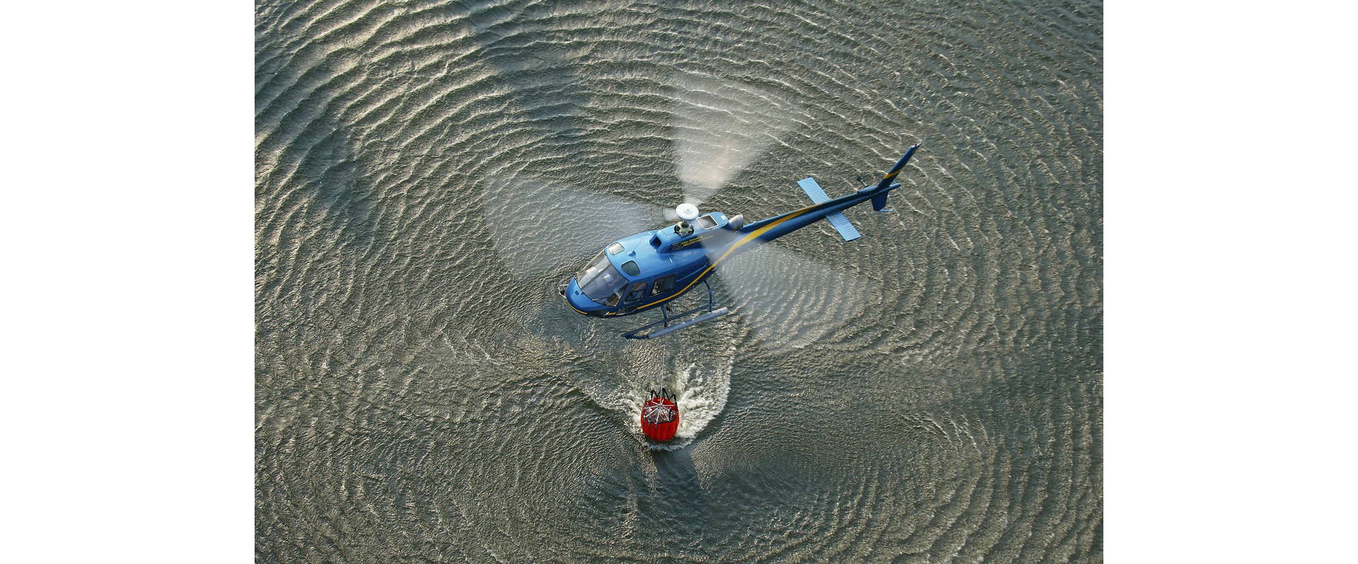 An Airbus-built helicopter loads its bucket-type water dispersal system in a dipping operation. 