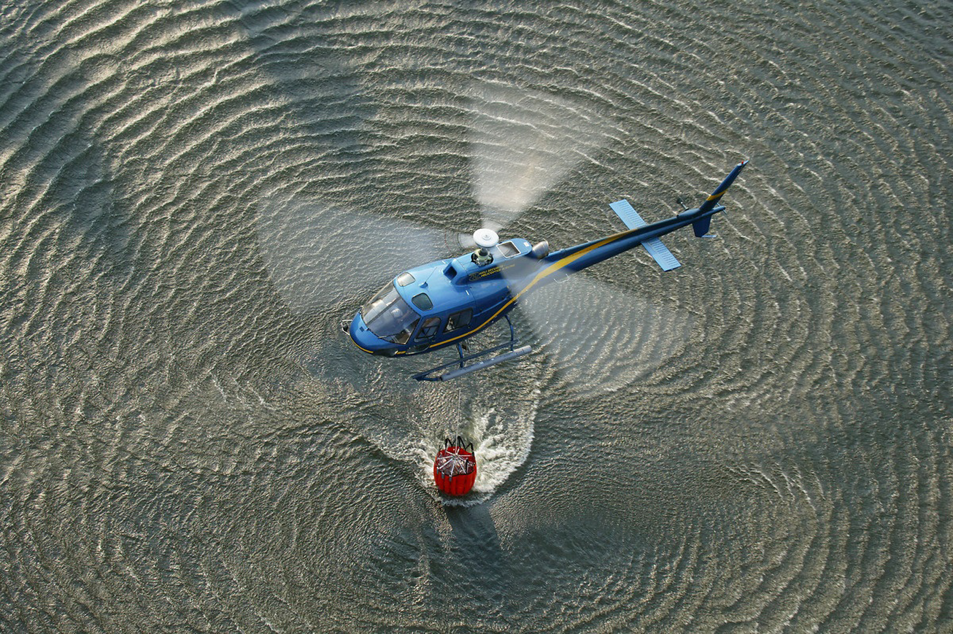 An Airbus-built helicopter loads its bucket-type water dispersal system in a dipping operation.