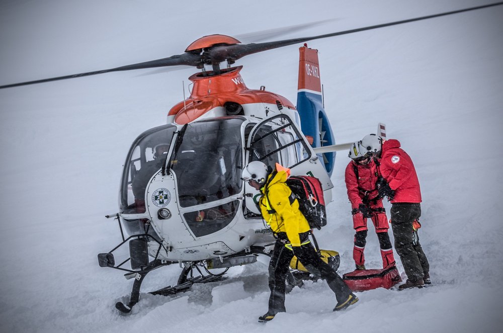 An Airbus H135 helicopter after landing in snowy conditions, with the pilot and crew on the ground  