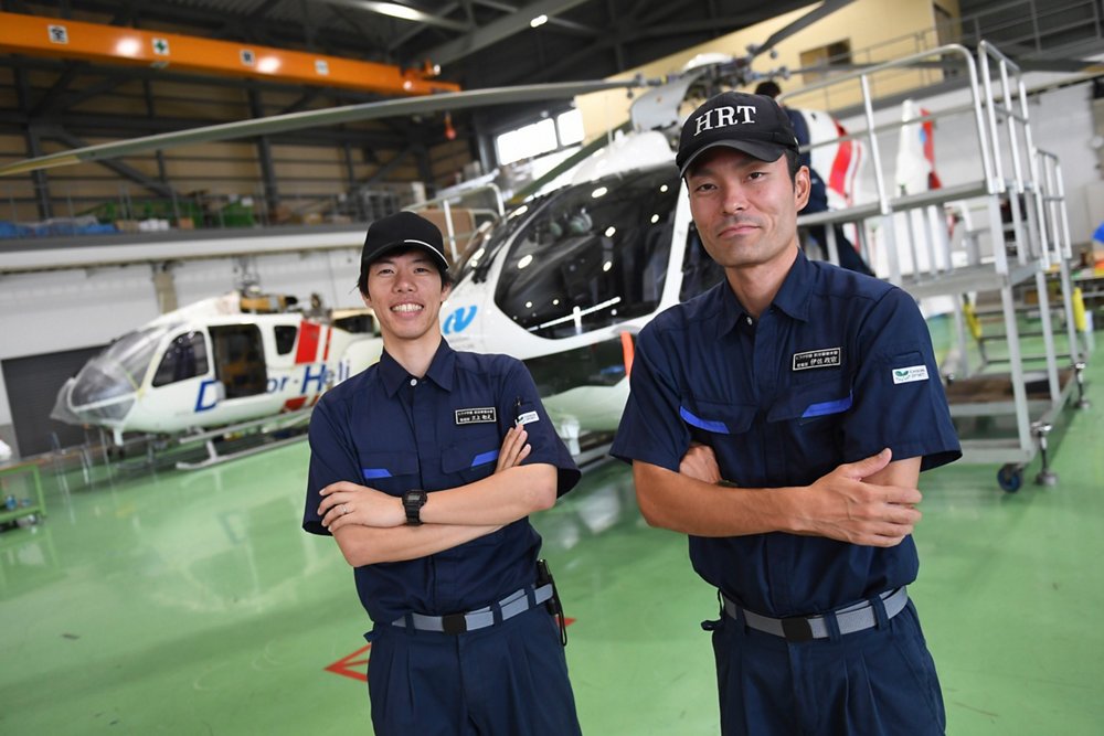 Two team members from Hirataguken pose in front of a pair of helicopters operated by the Japanese company. 