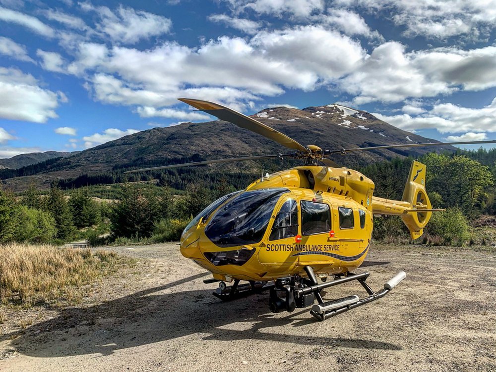 A parked H145 in the livery of Scottish Ambulance Service, with mountainous terrain in the background.