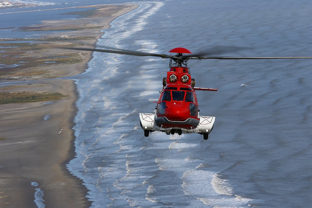 A head-on view of an Airbus-produced EC225 helicopter flying over a coastal setting.  