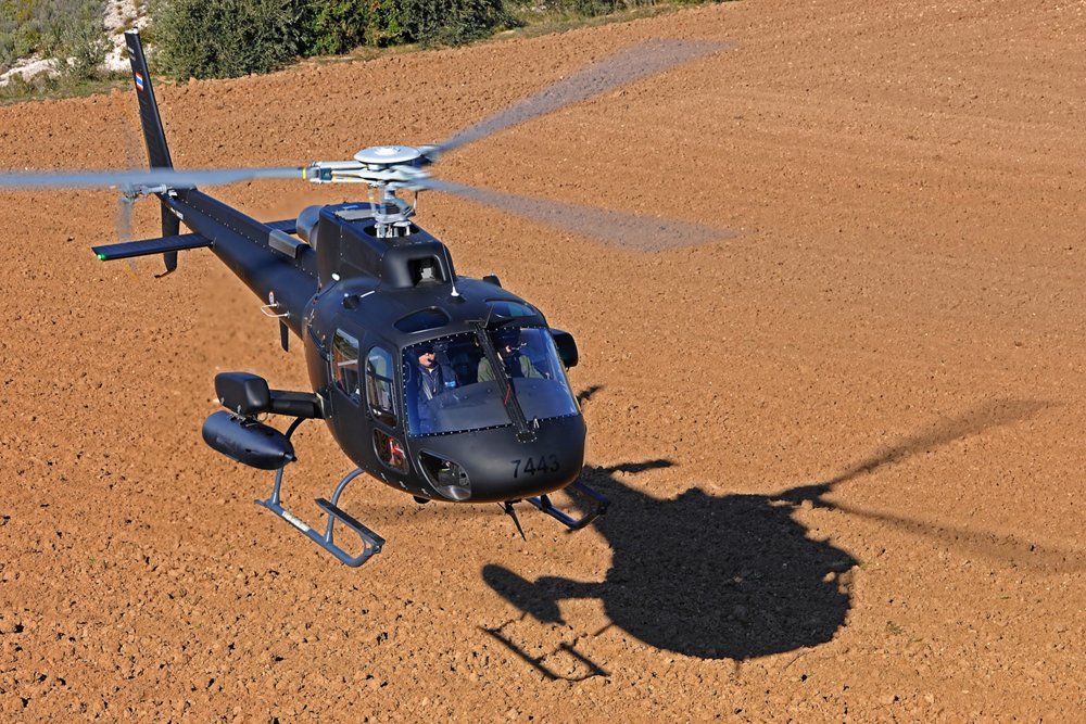 An Airbus H125M military helicopter configured for ISTAR (intelligence, surveillance, target acquisition, and reconnaissance) and attack missions hovers over the ground. 