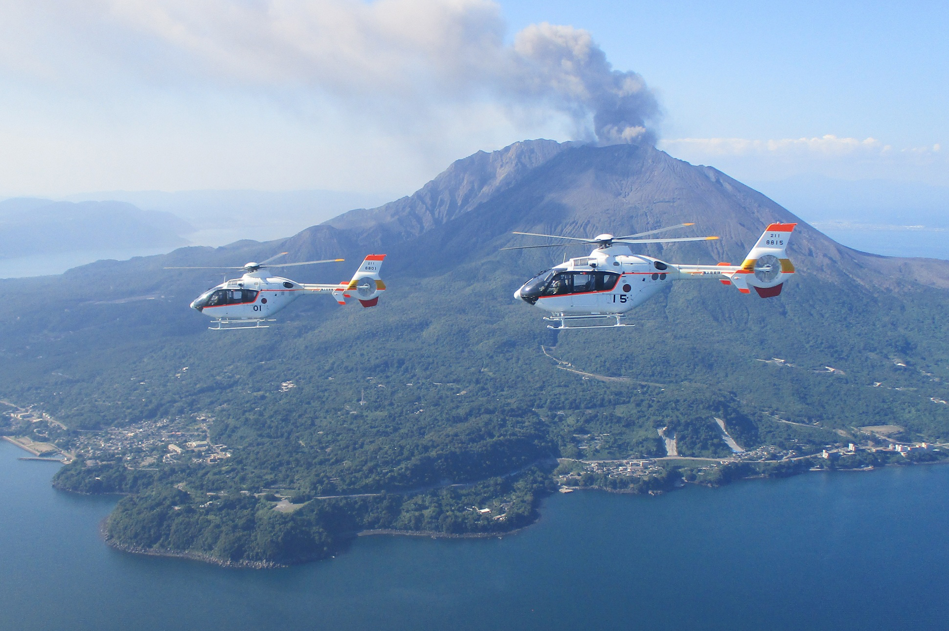 Two H135s operated by the Japan Maritime Self-Defense Force (JMSDF) fly near a volcano.