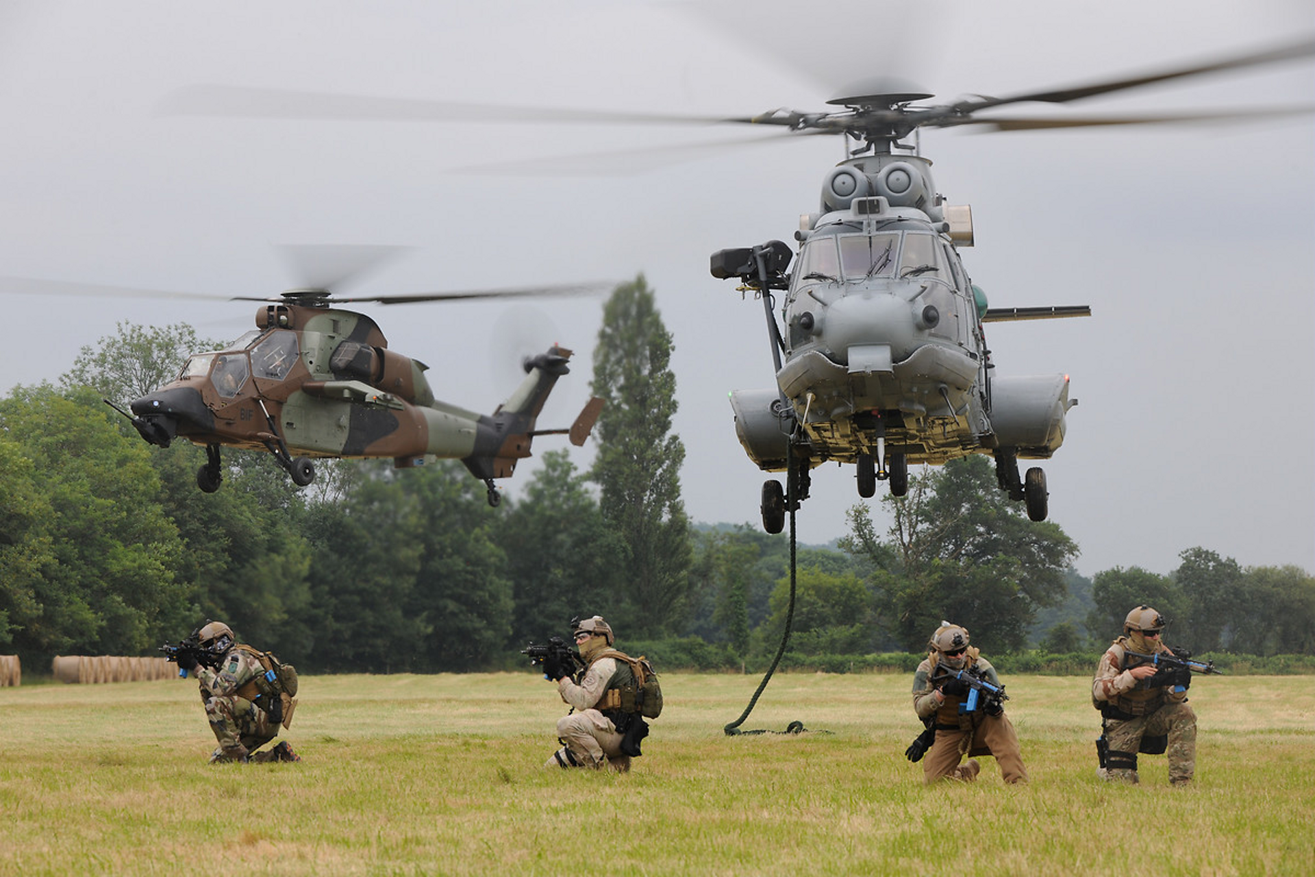 An H225M is shown during ascent with a Tiger HAD helicopter in the background.