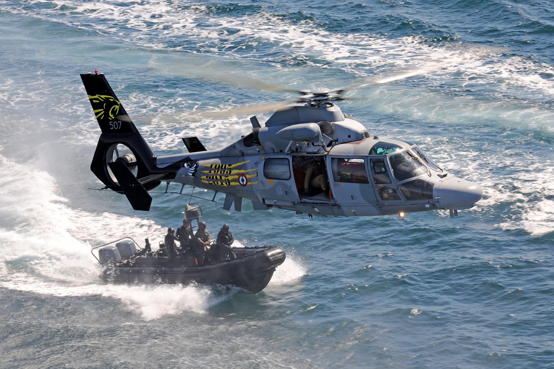 An Airbus AS565 MBe military helicopter of the French Navy flies over a vessel with commandos.